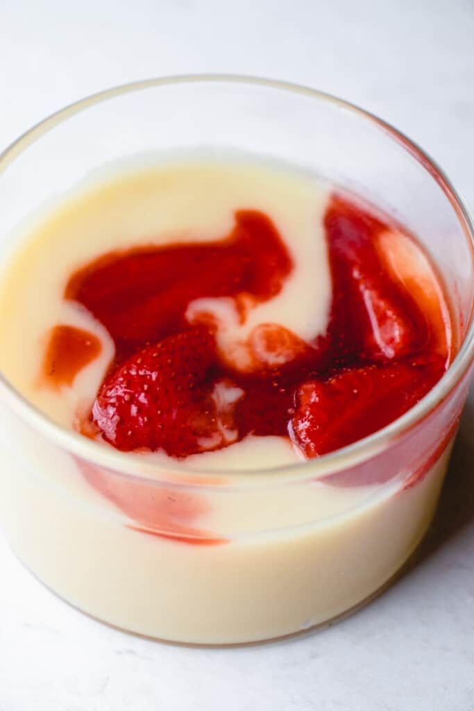 Close up shot of lemon custard drizzled with strawberry compote in a short glass jar.