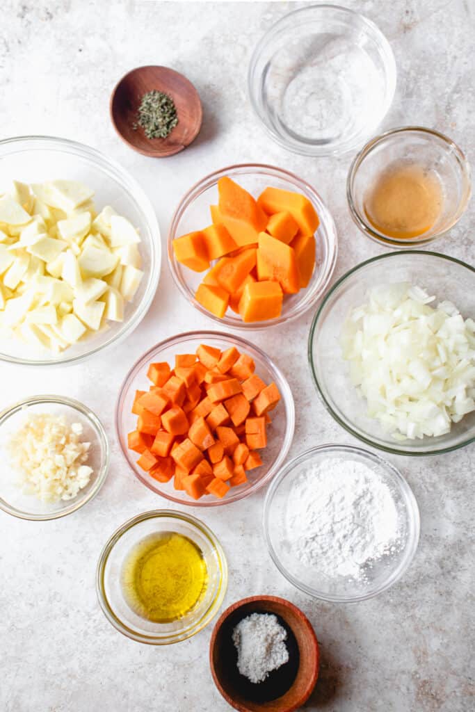 Mise en place of prep bowls with measured ingredients to make Vegan Queso Cheese Dip. Clockwise from top: water, apple cider vinegar, diced onions, tapioca starch, sea salt, extra virgin olive oil, crushed garlic, diced zucchini, dried thyme, diced butternut squash, and diced carrots.