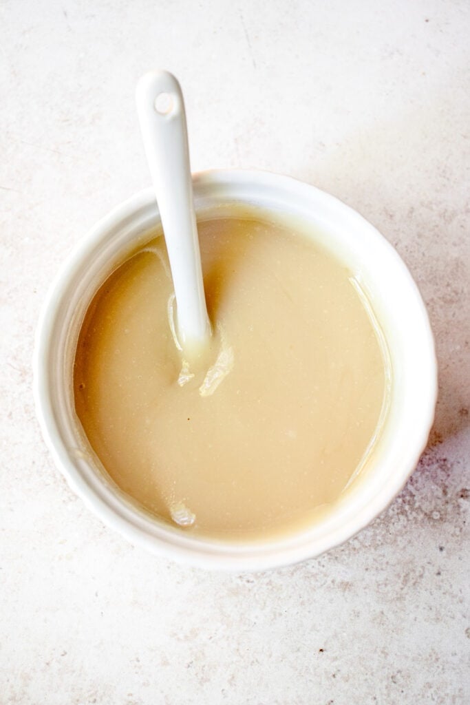 Maple glaze in a small white serving dish with a small white spoon sticking out.