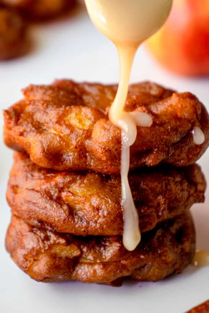 Close up shot of drizzling maple glaze over a stack of three Gluten Free Apple Fritters.