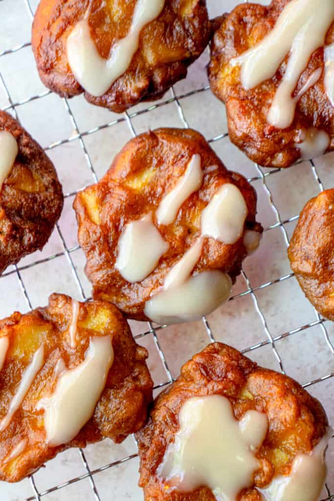 Maple glazed Gluten Free Apple Fritters on a wire cooling rack with parchment paper underneath.