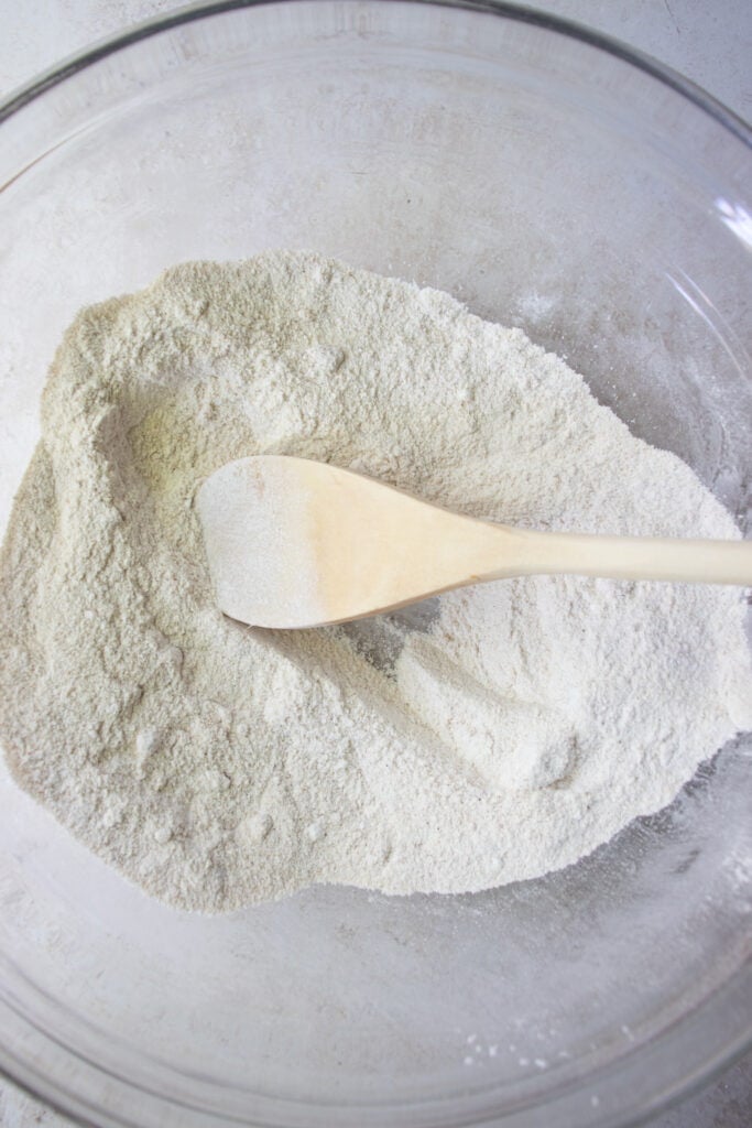 Dry ingredients and wooden mixing spoon in a large glass mixing bowl.