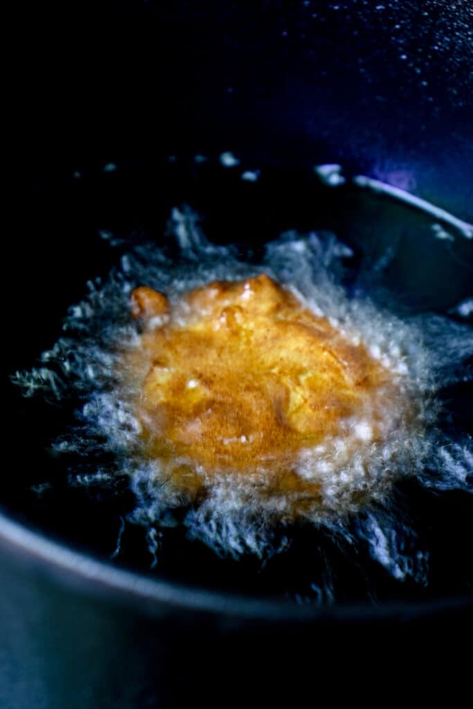 Apple fritter frying in oil in a deep cast iron pot.