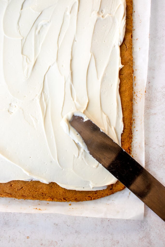 Pumpkin roll cake with cream cheese filling spread over it with an offset spatula.