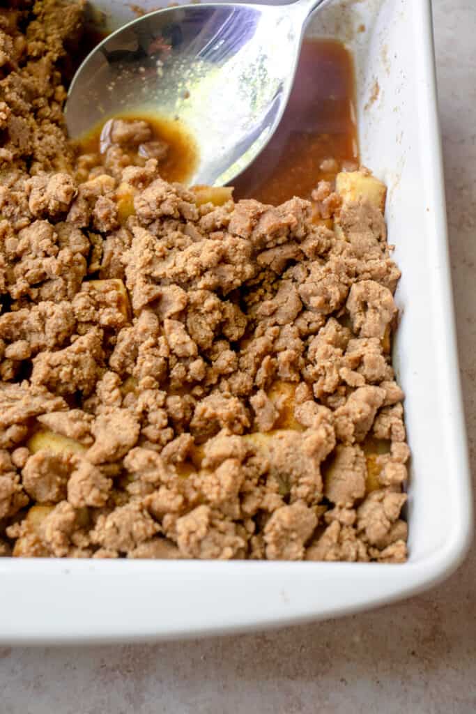 Baked apple crumble in a baking dish. A piece has been removed from the top right corner of the dish, where a large serving spoon rests.