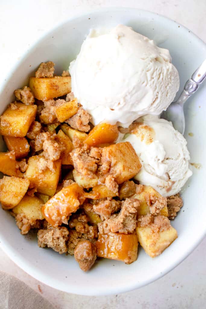 A bowl with apple crumble, scoops of dairy-free vanilla ice cream, and a spoon.