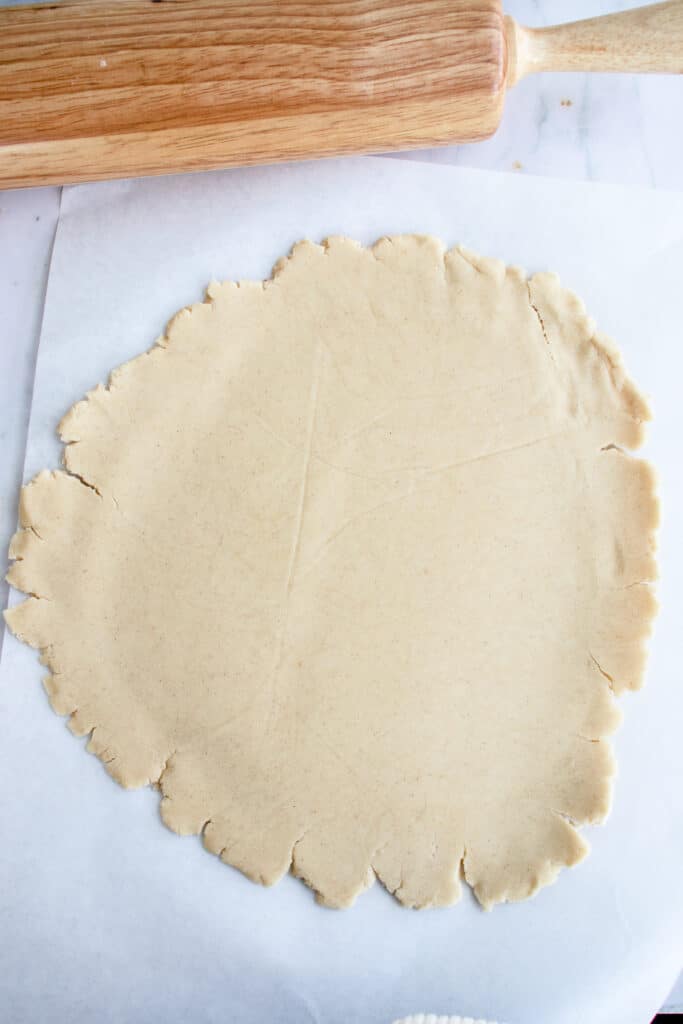 pie crust rolled out to 12 inches in diameter on a parchment paper with a rolling pin to the left of the dough