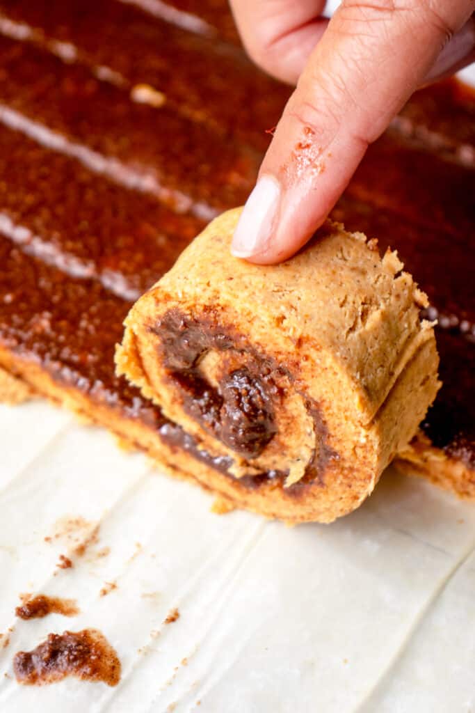 A close up of a Black hand rolling up an individual cinnamon roll.
