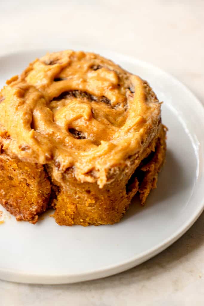 A small serving plate with a Gluten-Free Pumpkin Cinnamon Roll frosted with vegan pumpkin buttercream icing.