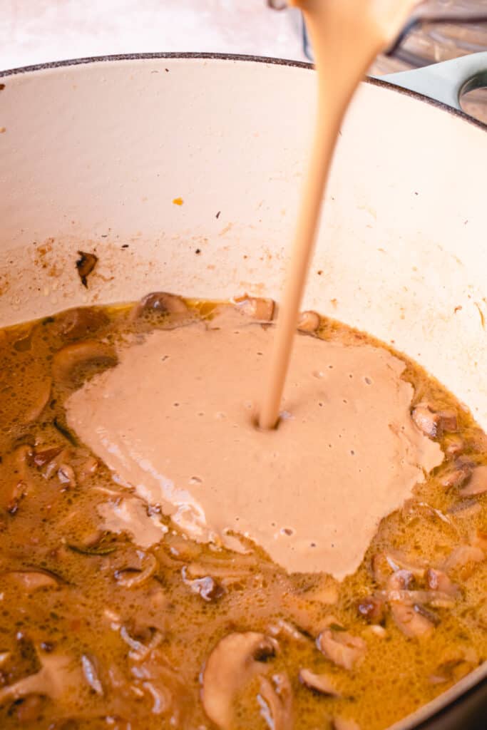 Puréed cream of mushroom soup being poured back into the pot with the remaining soup.