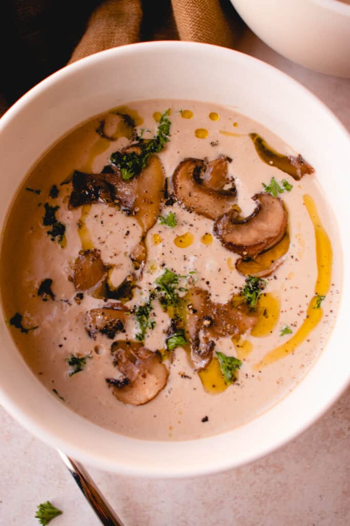 Gluten-Free Cream of Mushroom Soup garnished with olive oil, chopped parsley and ground black pepper.