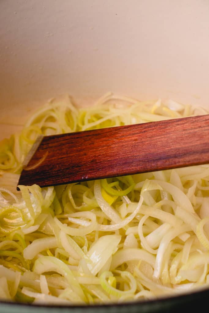 Leeks and onions sautéeing in a pot with a wooden flat sauté spatula.