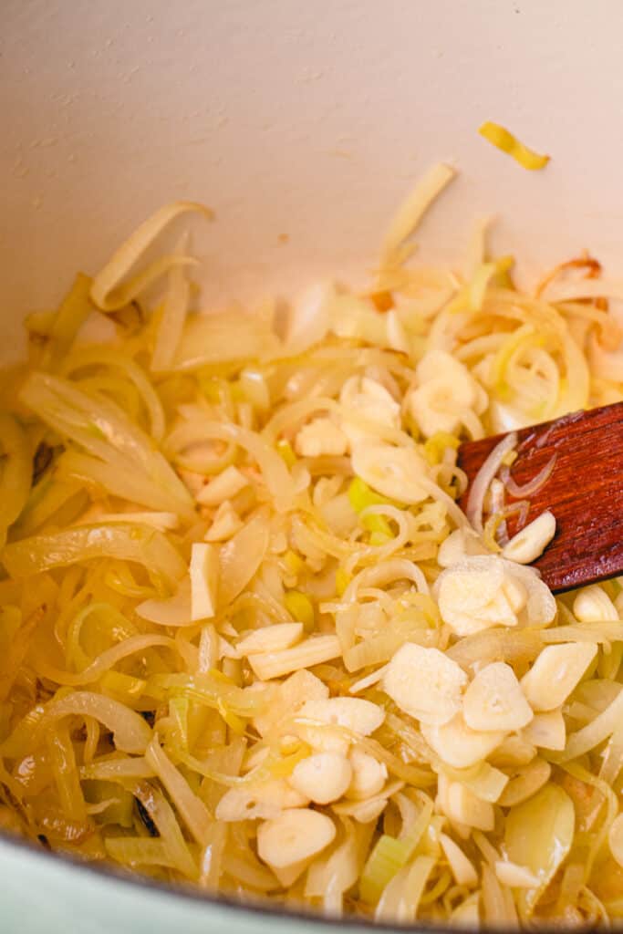 Onions, leeks and garlic in a pot with a wooden flat sauté spatula.