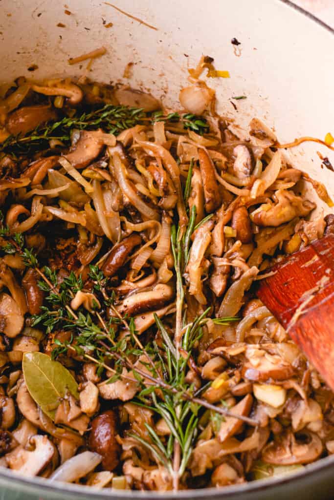 French oven with sautéeing onions, leeks, garlic, mushrooms, and sprigs of fresh rosemary, thyme, and two whole bay leaves.