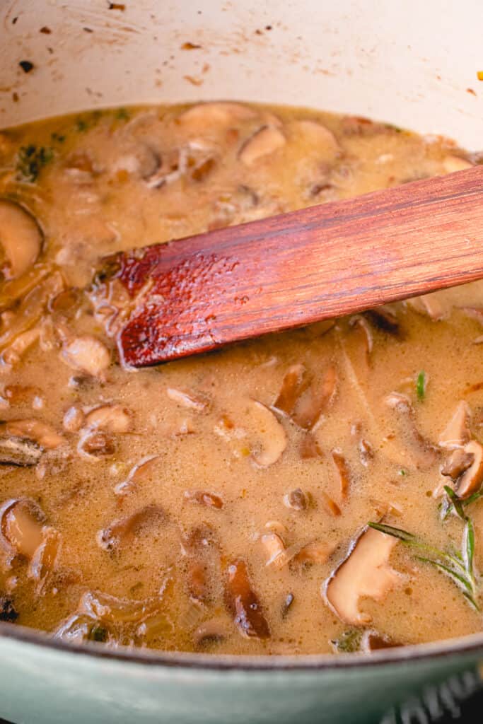Cream of mushroom soup ingredients a French oven with a wooden flat sauté spatula in the pot.
