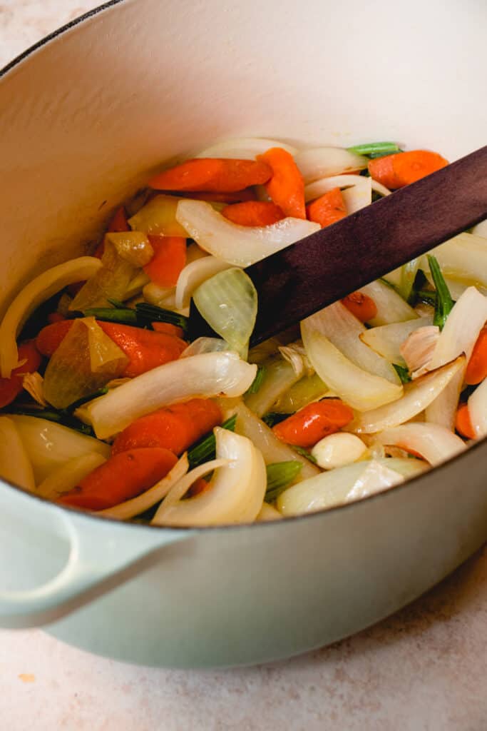 Sautéed vegetables in a large stockpot with a wooden sauté stick.