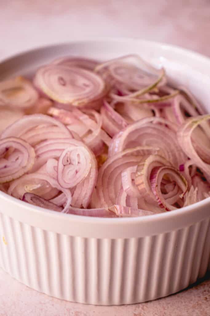 A white ceramic bowl with sliced shallots.