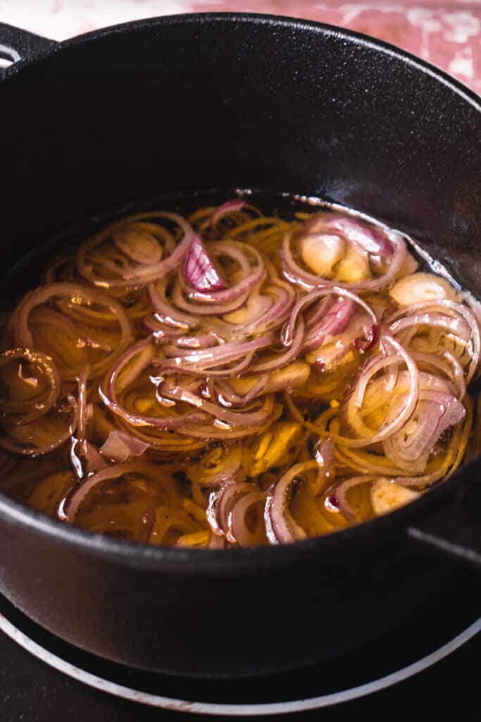 A black cast iron pot with avocado oil and shallots on a hot plate.
