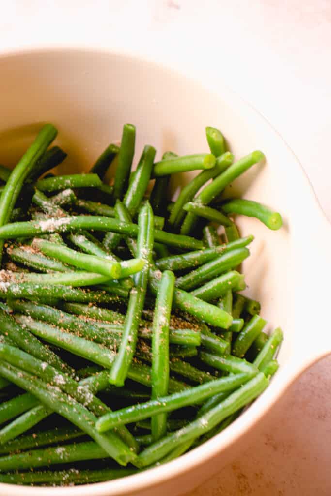 A large mixing bowl with blanched green beans, sea salt and black pepper.