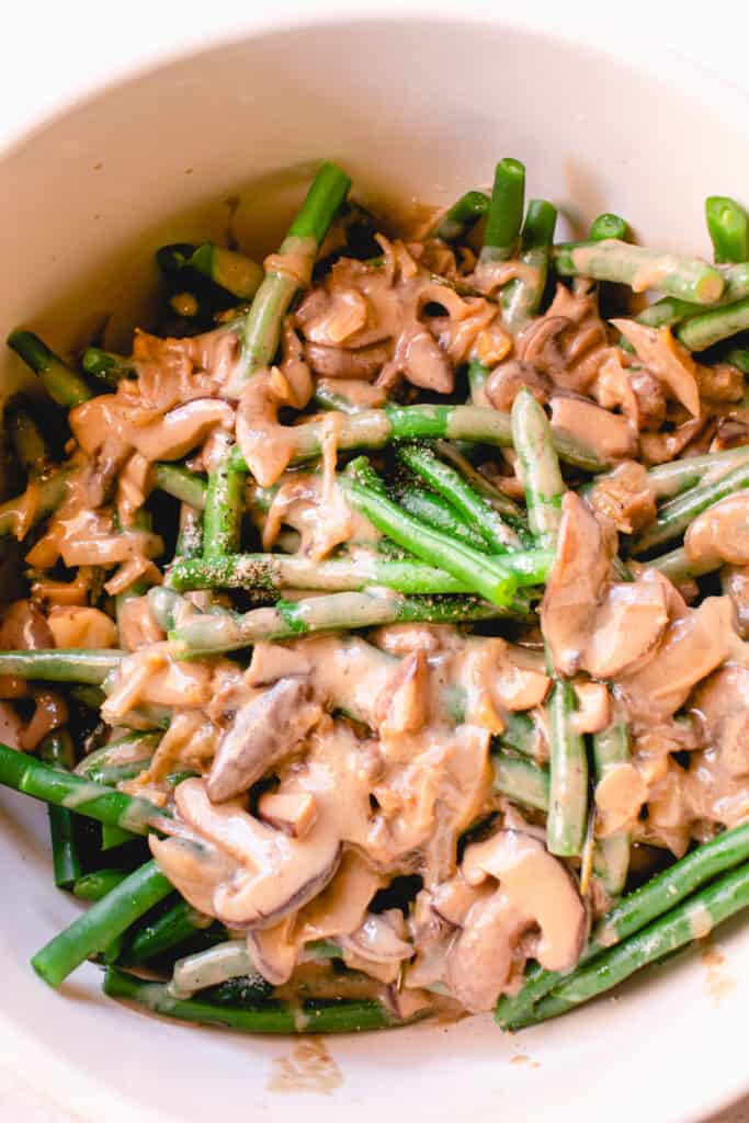 A large mixing bowl with blanched green beans, sea salt, black pepper, and cream of mushroom soup.