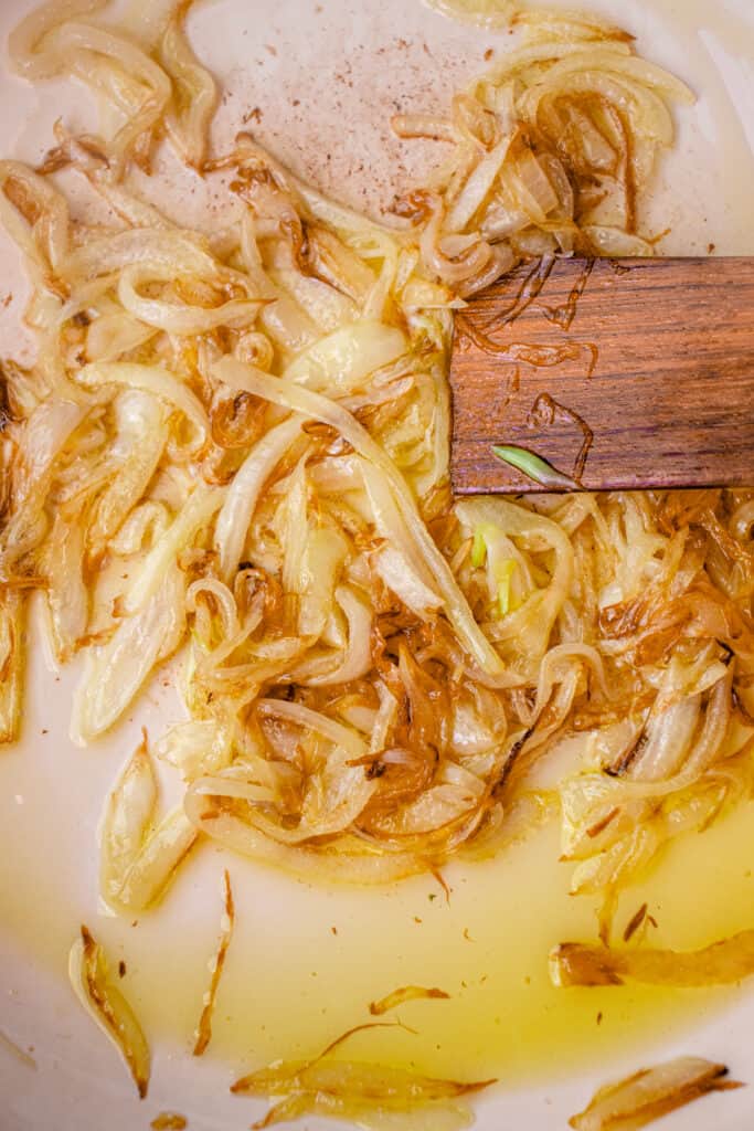 Onions caramelizing in a skillet, with a wooden stirring stick in the pan.
