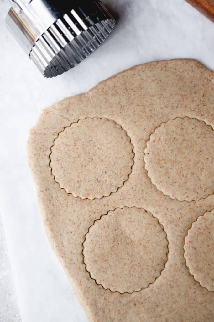 Rolled out sheet of cookie dough with cookies cut out, a rolling pin, and a cookie cutter, on top of a sheet parchment paper.