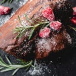 Decorated Gluten-Free Yule Log on a slate serving board. Garnished with raspberries, sprigs of fresh rosemary and dusted with sifted arrowroot starch.