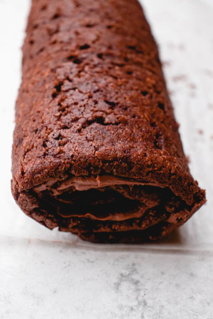 Rolled up chocolate sponge cake with chocolate filling on a piece of parchment paper.