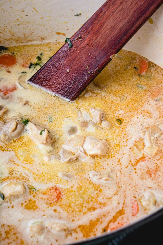 The flat wooden sauté spatula stirs the soup in a French oven.