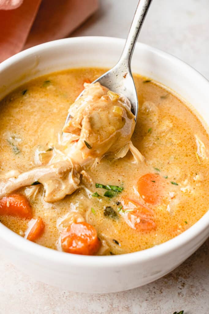 A spoon lifts out a piece of chicken from a bowl of the Creamy Chicken Soup.