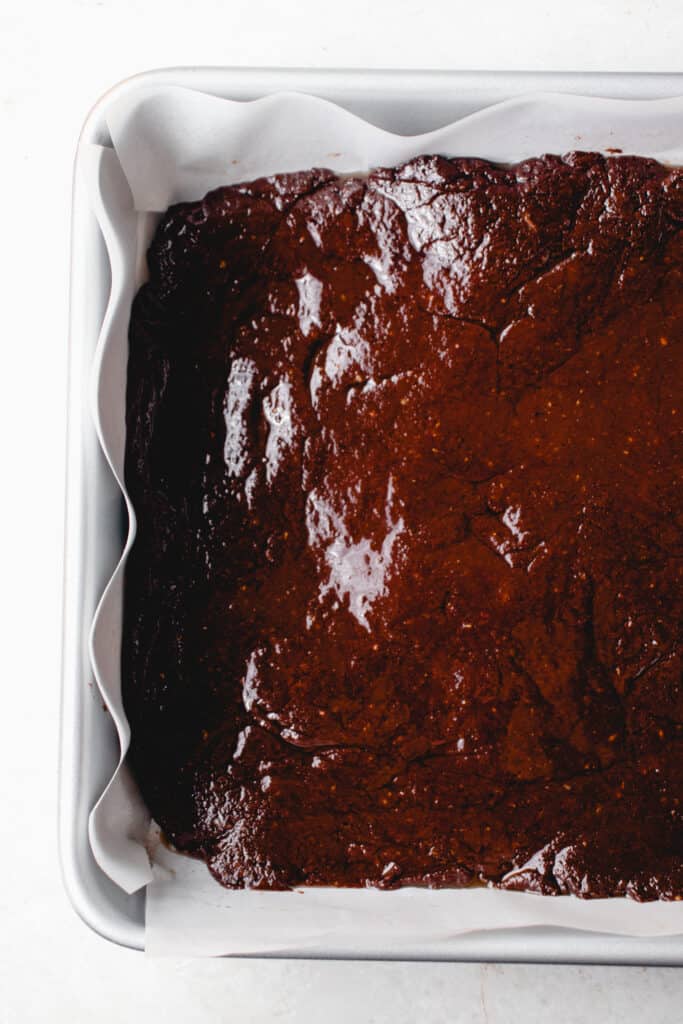 Gluten-Free Vegan Brownie batter poured into a parchment paper lined square baking pan.