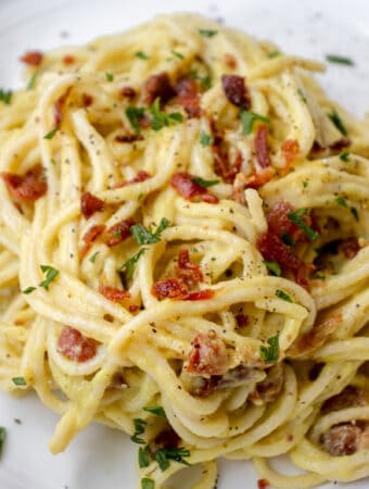 white plate with pasta carbonara made of spaghetti with crumbs of bacon, garnished with parsley and black pepper.