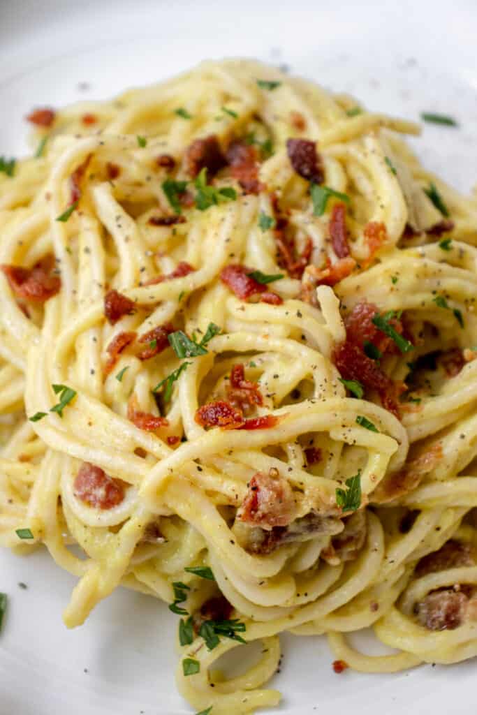 white plate with pasta carbonara made of spaghetti with crumbs of bacon, garnished with parsley and black pepper.