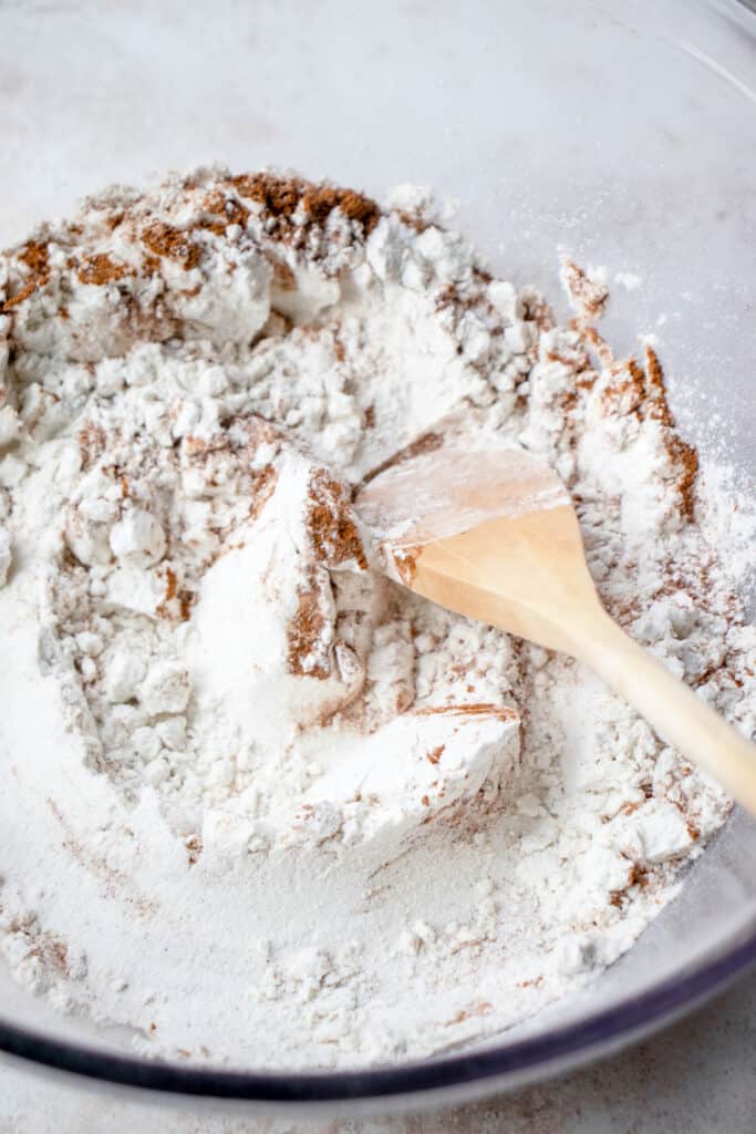 Close up of a large glass bowl with dry ingredients and a wooden spoon.