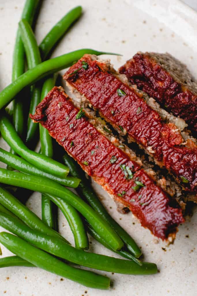A plate with three slices of Dairy-Free Gluten-Free Meatloaf and green beans.