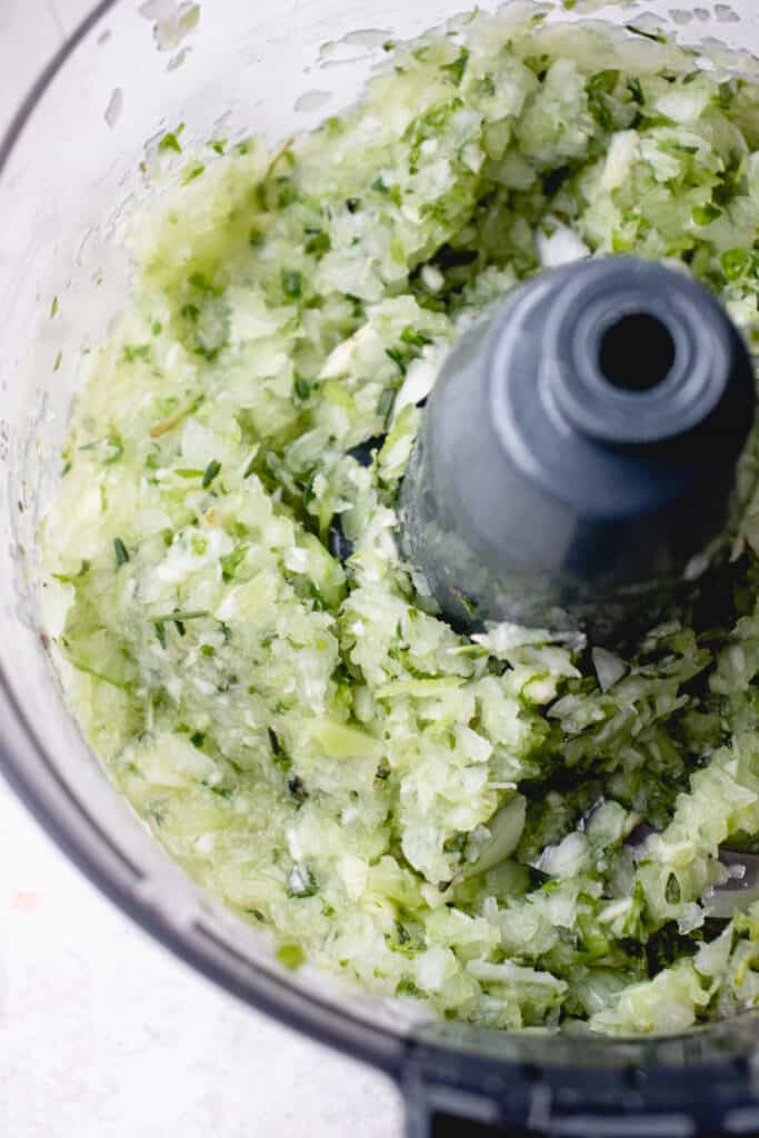 A food processor with pulsed fresh herbs, onion, garlic, and celery.