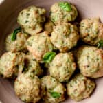 A bowl with baked Gluten-Free Meatballs garnished with fresh basil leaves.