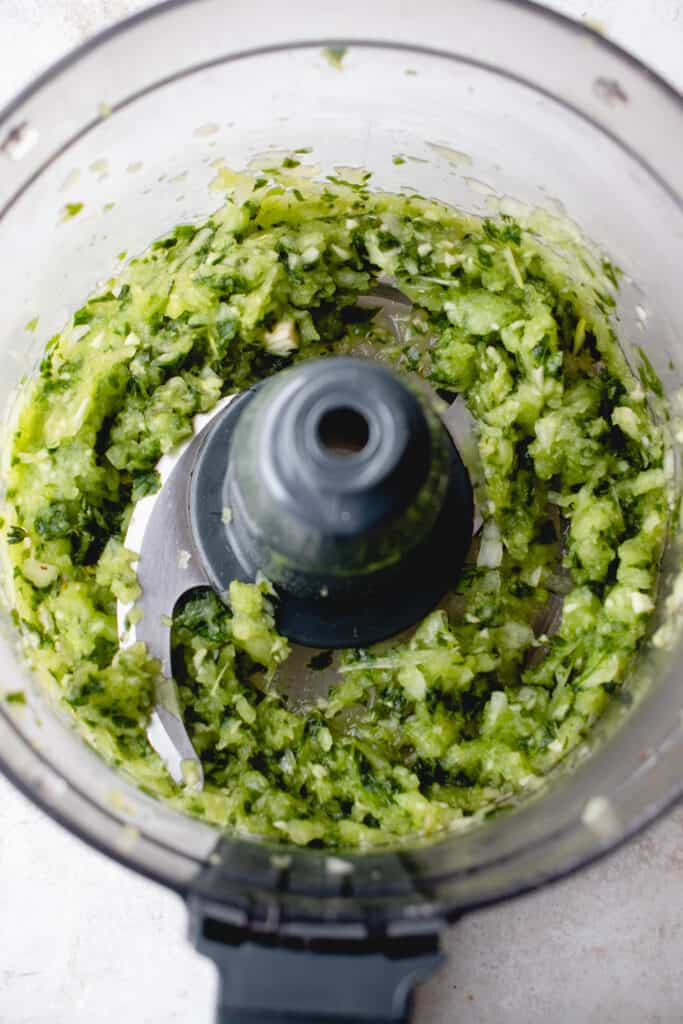 A food processor with pulsed fresh herbs, garlic, and onion.