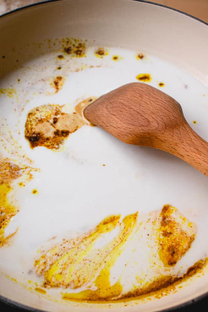 Coconut milk, sea salt and apple cider vinegar added to the bloomed spices in the skillet, stirred with a wooden spatula.