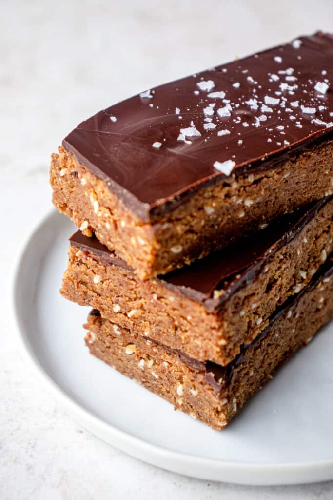 A stack of 3 rectangular Gluten-Free Dairy-Free Protein Bars on a small white plate, topped with flaky sea salt.