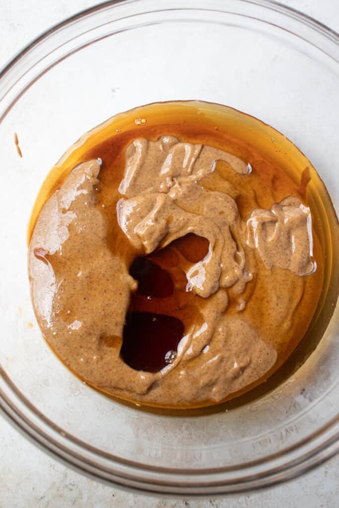 A large glass bowl with almond butter, maple syrup, and vanilla extract.