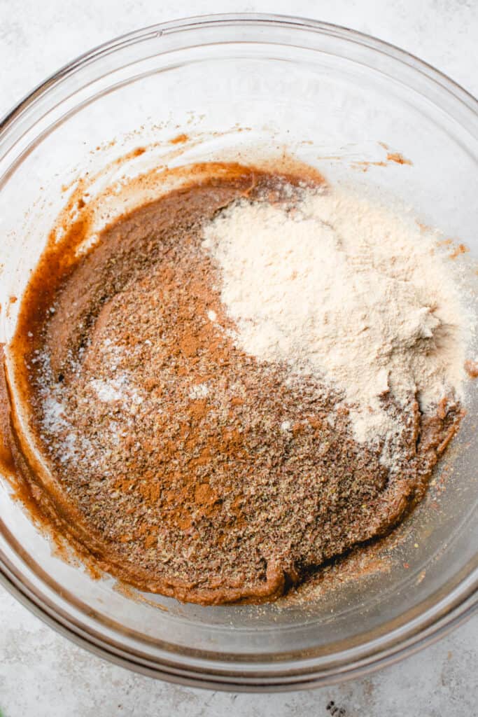 Flaxseed meal, cinnamon, sea salt, and protein powder added to the liquid ingredients in a large glass bowl.
