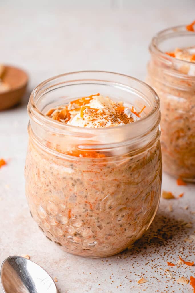 Two glass mason jars with Vegan Carrot Cake Overnight Oats and additional toppings.