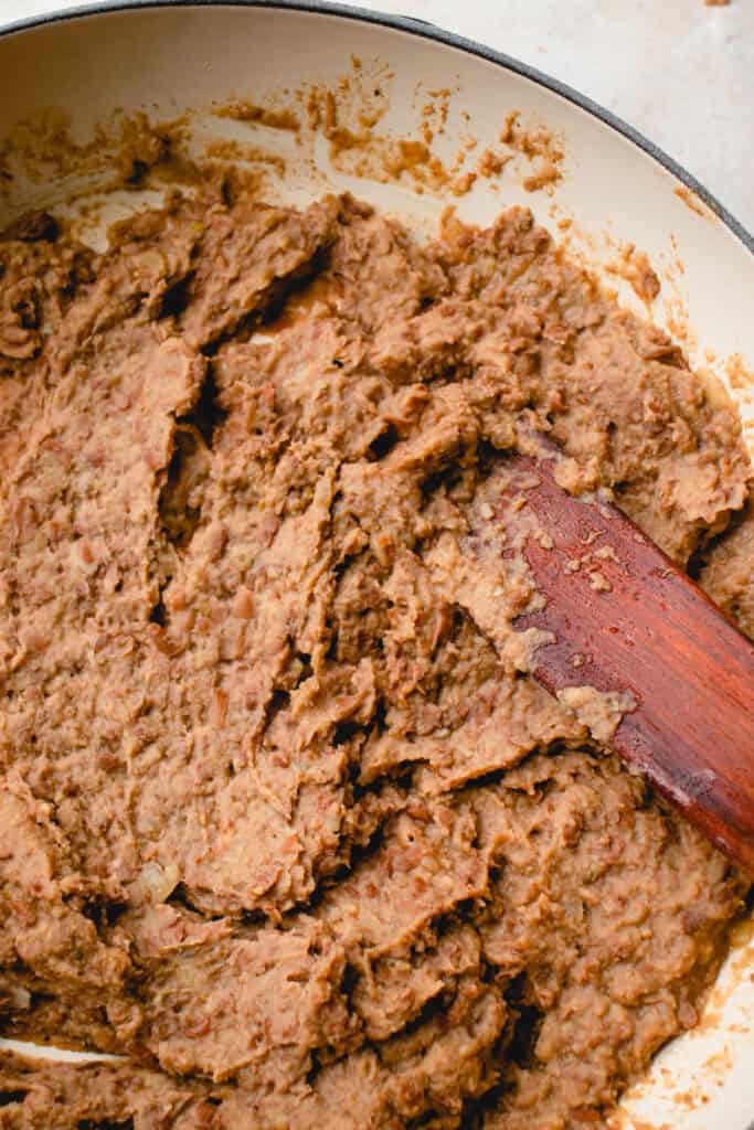 The mashed pinto beans in the skillet, stirred and smoothed with a wooden sauté stick, to make homemade refried beans.