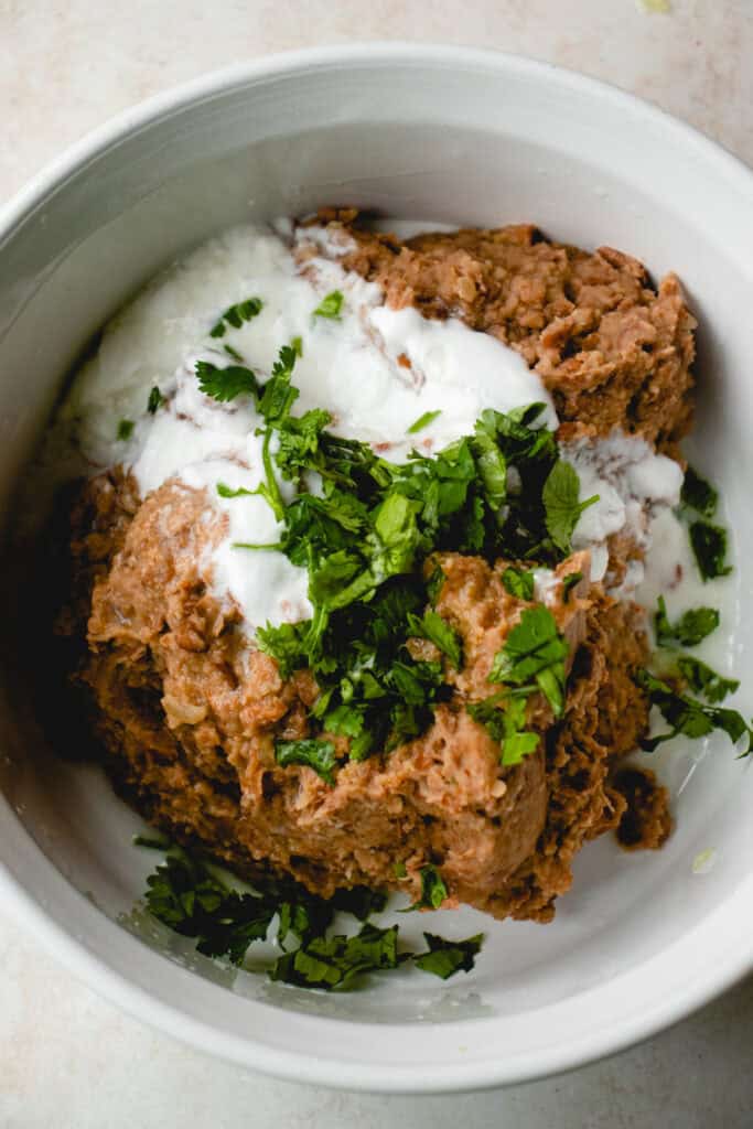 A bowl with mashed pinto beans, coconut yogurt, lime juice, and chopped cilantro.