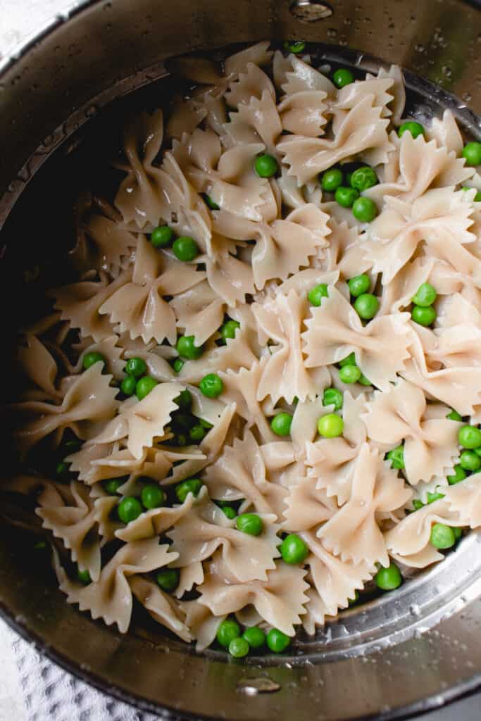 Drained and rinsed gluten-free pasta and green peas in a pot.