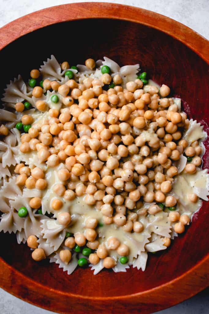 Gluten-free pasta, green peas and chickpeas marinate in the dressing in a wooden salad bowl.