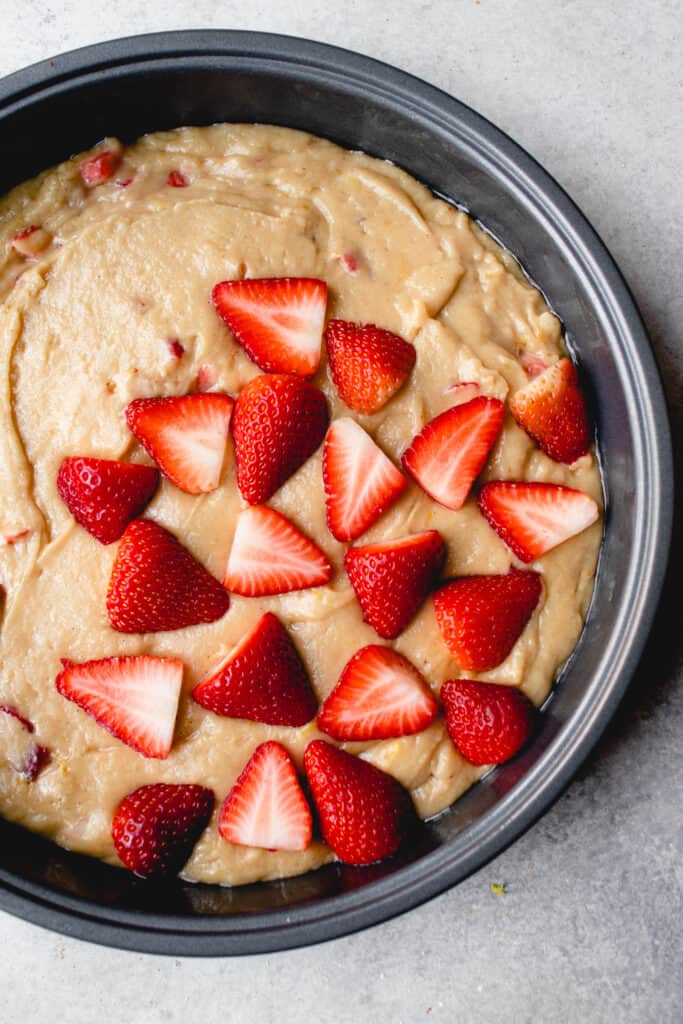 Halved strawberries are placed on top the batter in the cake pan.