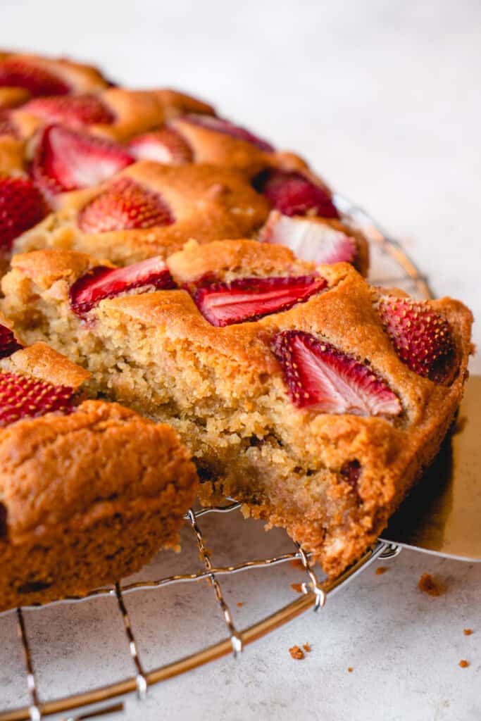 A cross-section view of a slice of Gluten-Free Strawberry Cake as it is lifted out of the cake on top of a wire cooling rack.