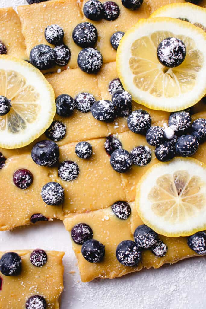 Set Gluten Free Lemon Blueberry Bars sliced into squares, garnished with lemon slices and sifted powdered sugar.